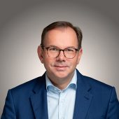 Portraitfoto von Mathias Wagner vor grauem Hintergrund.